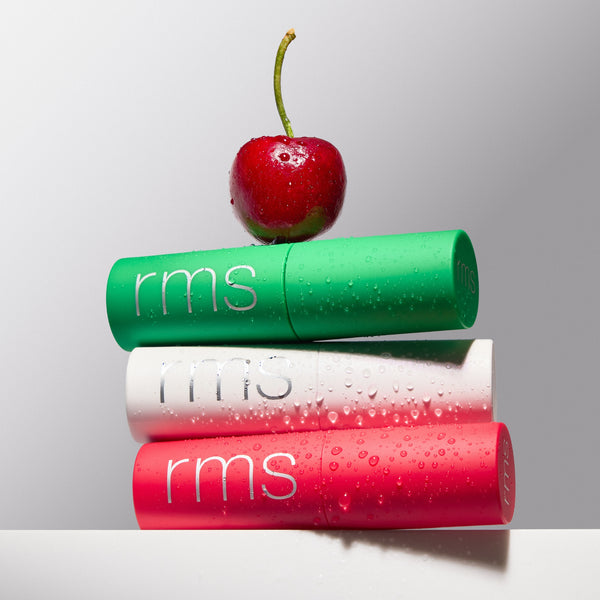 Three RMS beauty products stacked with a cherry on top against a light background