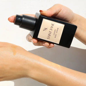 Hand applying Saint Jane luxury body serum to a person's arm with a neutral background. SAINT JANE Luxury Body Serum Nourishing Body Serum