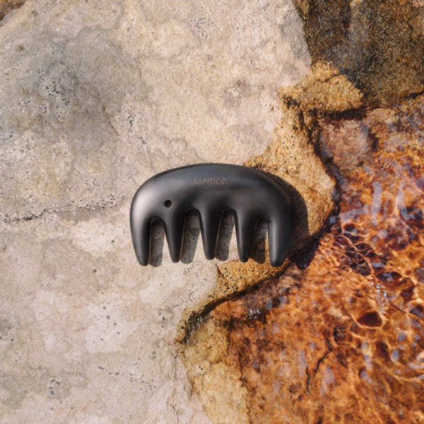 Black gua sha tool on a textured stone surface