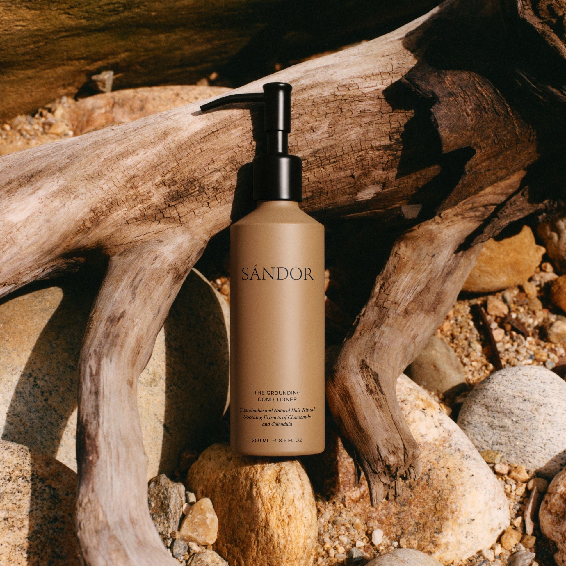 SANDOR bottle of conditioner with a black pump on a natural background with wood and stones
