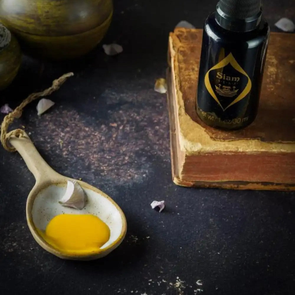 Black glass bottle with a pump of SIAM SEAS Twilight BeCalm Skin Serum next to a spoon with a serum texture on a dark surface