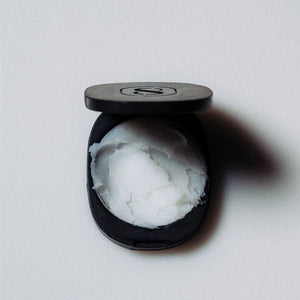 Black compact with white balm perfume inside on a light gray background