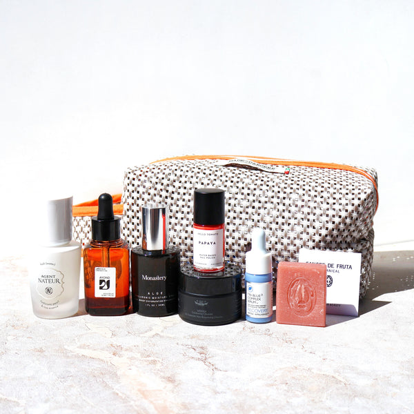 Collection of skincare and cosmetic products with a patterned pouch on a light background