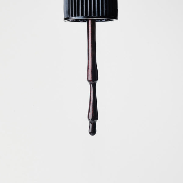 Black dropper with a drop of dark red nail polish on a light gray background