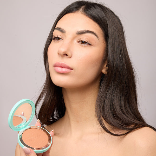 Woman holding a makeup compact with a neutral background
