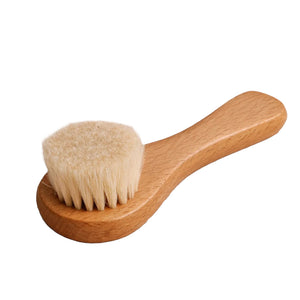 A small wooden face brush with a light natural wood handle and soft cream-colored bristles, shown on a plain white background.
