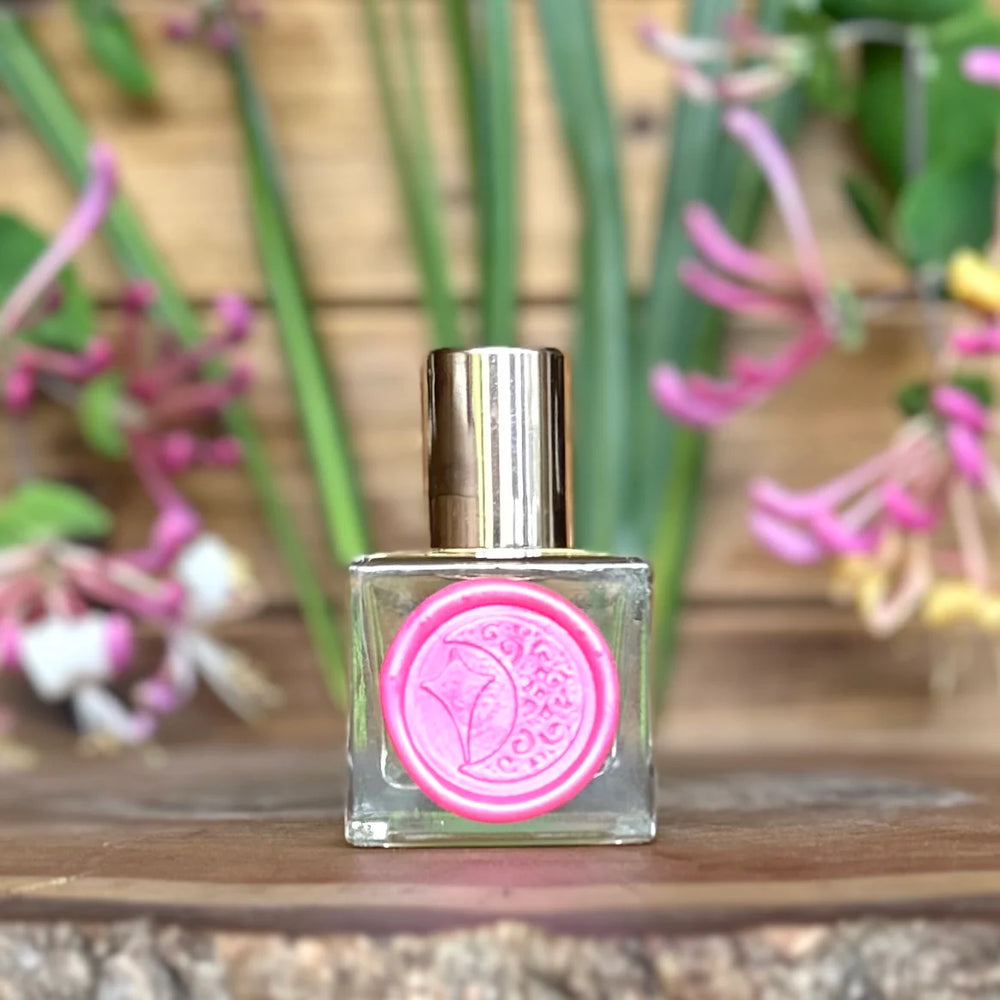 Paradise perfume oil bottle and packaging by The Potion Cosmetics on a wooden surface with a blurred natural background