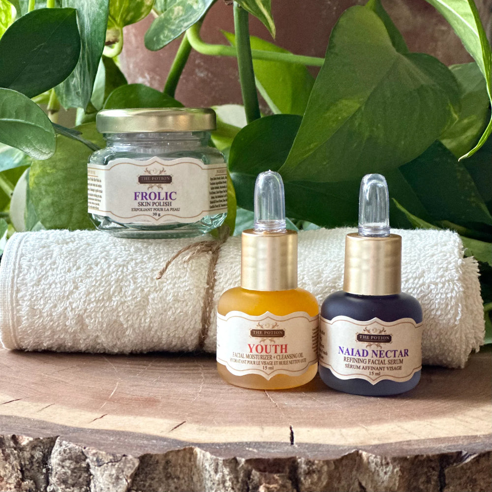 THE POTION COSMETICS The Glow Collection featuring Youth Face Potion, Naiad Nectar Refining Serum, Frolic Skin Polish, and an organic cotton face cloth arranged elegantly to highlight a radiant, glow-enhancing skincare routine.