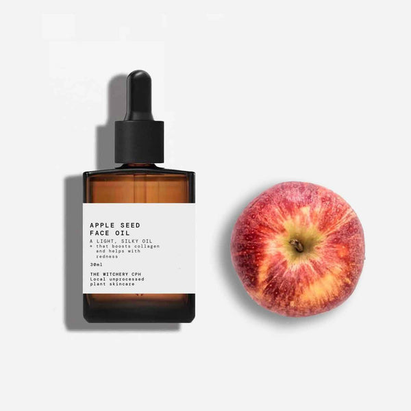 Apple seed face oil bottle with a dropper next to an apple on a white background