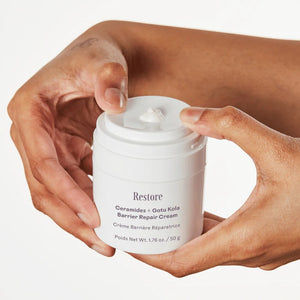 A person's hands holding a white jar of Restore Ceramides + Gotu Kola Barrier Repair Cream against a clean white background.