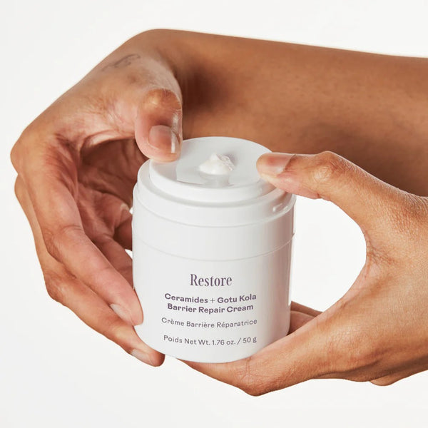 A person's hands holding a white jar of Restore Ceramides + Gotu Kola Barrier Repair Cream against a clean white background.