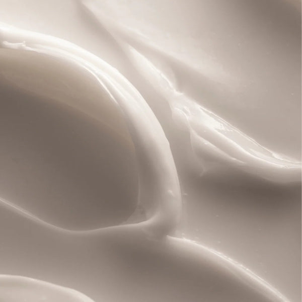 A close-up texture shot of a thick, creamy off-white face cream with smooth, glossy swirled ridges.