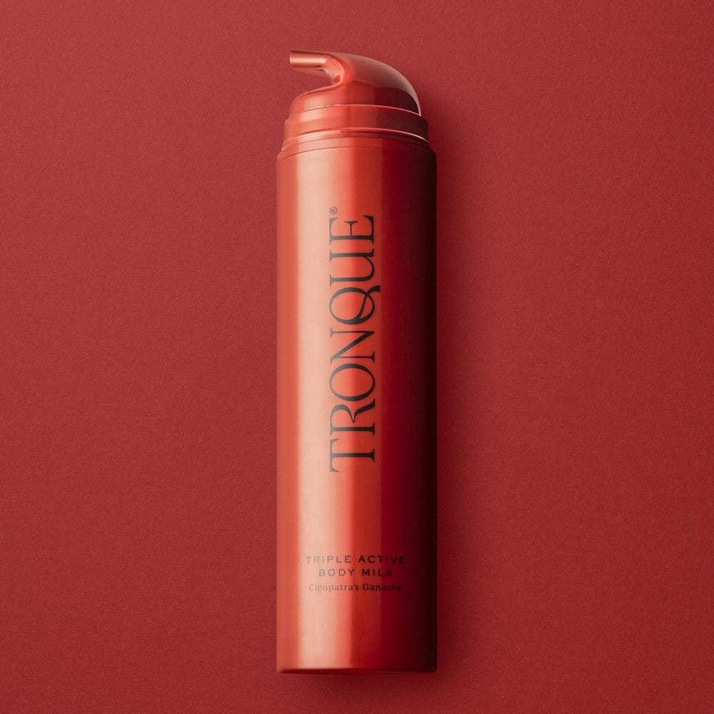 Red bottle of TRONQUE body milk on a white background. TRONQUE Triple Active Body Milk