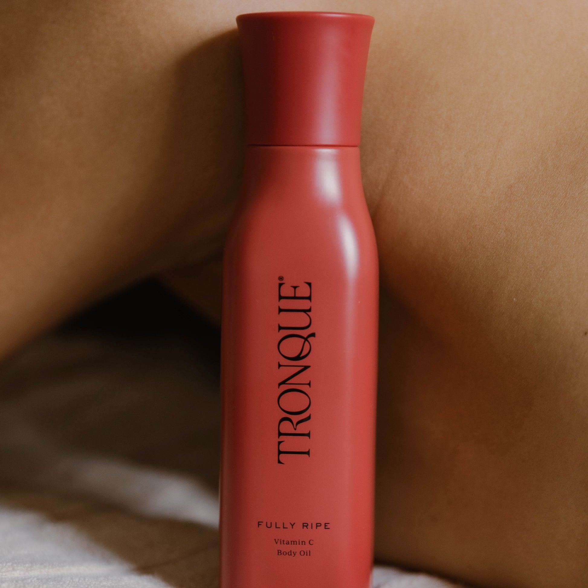 Red bottle of TRONQUE skincare product. TRONQUE Vitamin C Body Oil