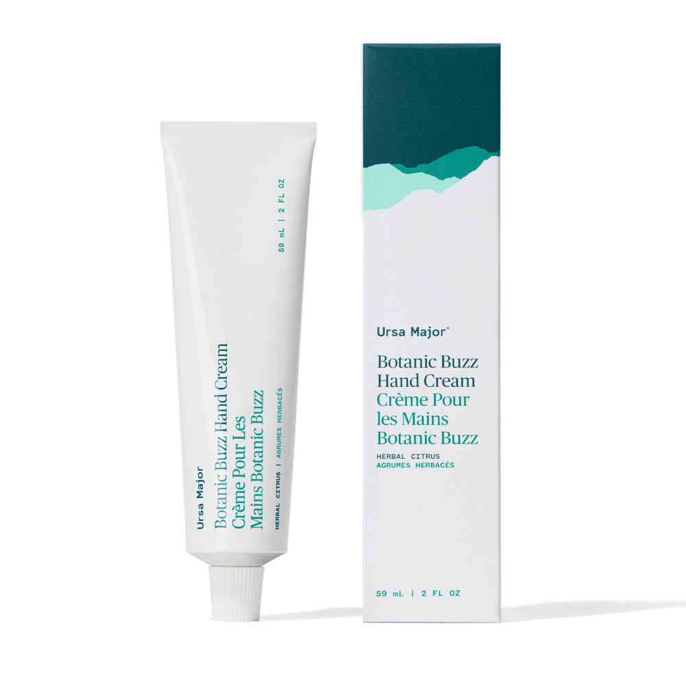  A sleek aluminum tube of Ursa Major Botanic Buzz Hand Cream, surrounded by natural elements like pine, cloudberry, and lavender. The packaging hints at forest botanicals and a clean, uplifting skincare experience.