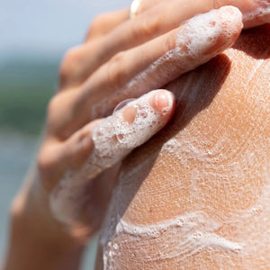 Hand applying soap to another hand with a blurred natural background