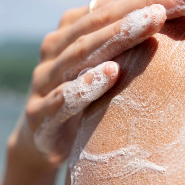 Hand applying soap to another hand with a blurred natural background