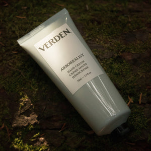A tube of Verden Arborealist hand cream lies diagonally on a mossy, forest floor background.
