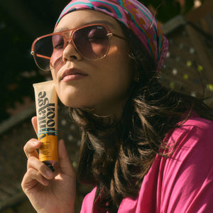 Woman wearing sunglasses and a colorful headscarf, holding a tube of VINTAGE NOON Vacation Skin Overnight Mask and Moisturizer.
