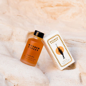 Orange face oil bottle by Wonder Valley and white box with gold design on a beige textured background