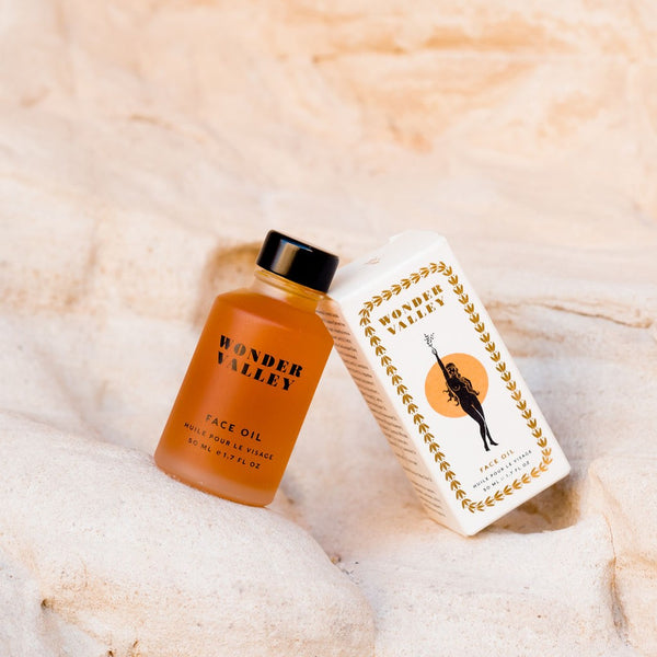 Orange face oil bottle and white box with gold design on a beige textured background