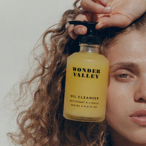 Person holding a bottle of Wonder Valley Oil Cleanser near her face.