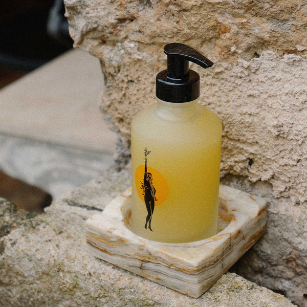 Yellow bottle with black pump on a stone coaster against a stone wall.