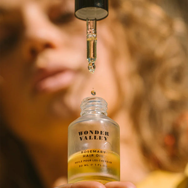 Wonder Valley rosemary hair oil with a dropper being used.