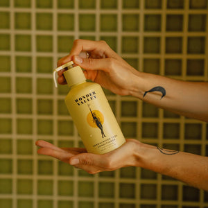 Person holding a bottle of Wonder Valley hair conditioner against a tiled wall background