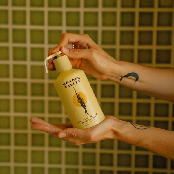 Person holding a bottle of Wonder Valley hair conditioner against a tiled wall background