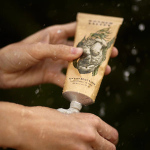Hand holding a tube of body scrub with a design on the label against a dark background