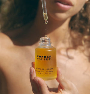 Person holding a bottle of 'Wonder Valley' wonder serum with a dropper.