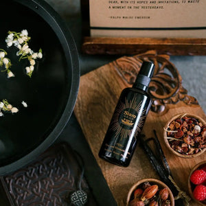 Black bottle with gold label of SIAM SEAS Yen Essence Toner on a wooden surface with flowers and books in the background. ALWAYS SHOW