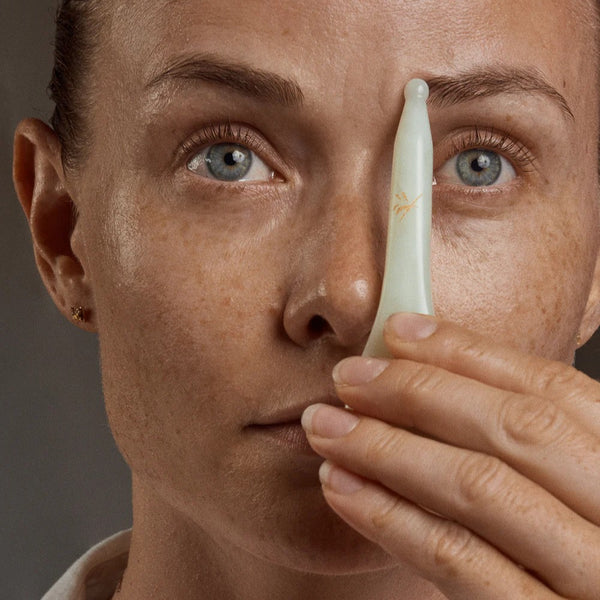 woman holding a skincare tool near their eye against a neutral background. YIN YOUR SKIN NIVA Gua Sha Beauty Spoon
